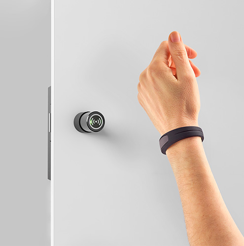 Eine Hand nähert sich mit einem RFID-Armband kontaktlos einem Ojmar-Schließzylinder an einer Umkleidetür